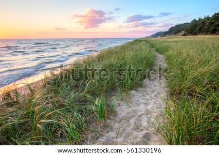 A Walk On The Beach. Sandy path winds along the shore of Lake Michigan with a sunset horizon and sand dunes as a backdrop. Muskegon, Michigan Royalty-Free Stock Photo #561330196