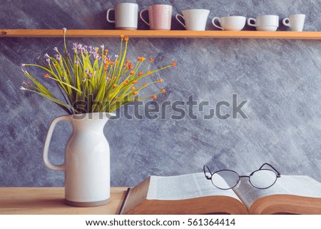 Old book with reading glasses on table and flower in jug