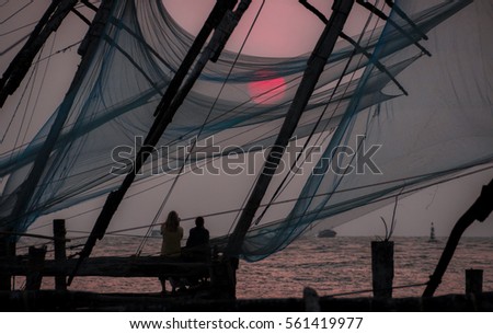 Chinese fishing nets on the shore of the Arabian Sea. Fort Cochin, Kerala, India. Historic Landmark. Warm evening. Scenic contours in the sunset twilight. Bright solar disk. Delicate juicy colors.