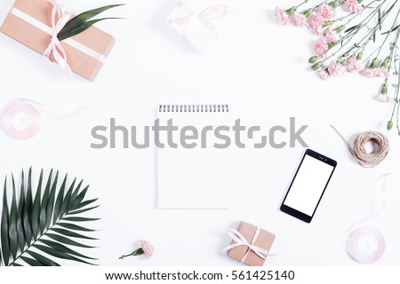 Festive arrangement: boxes with gifts, ribbons, notebook, mobile phone and flowers lie on a white table, top view Royalty-Free Stock Photo #561425140