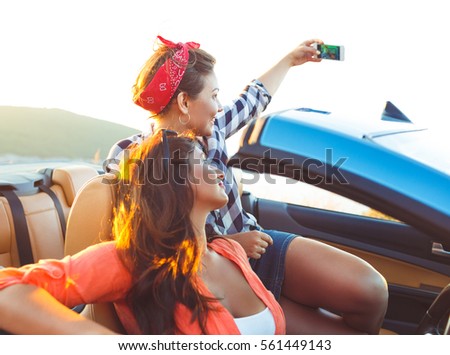 Two young beautiful girls are doing a photo of yourself in a convertible