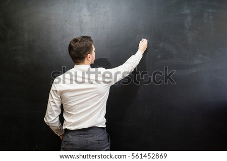 Man in suit pointing something on chalkboard,back view,isolated.Copyspace blank.Teacher writing on black board