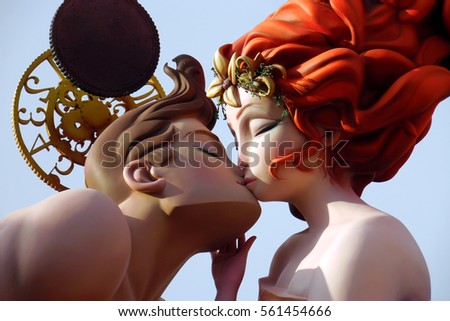 Colorful giant papier mache figures kissing in Fallas festival of Valencia, sculpture of ninots under blue sky. Couple kiss. Girl with red hair kissing boy with brown hair.