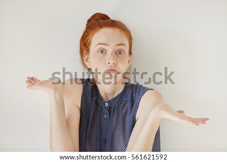 Puzzled and clueless young redhead woman with arms out, shrugging her shoulders, saying: who cares, so what, I don't know. Negative human emotions, facial expressions, life perception and attitude Royalty-Free Stock Photo #561621592