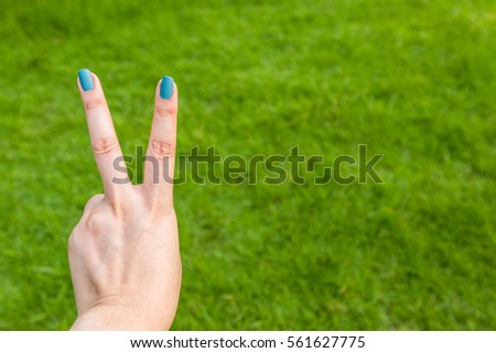 Women hold two fingers on green grass background texture