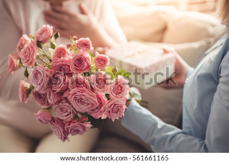 Cropped image of beautiful adult woman giving flowers and a gift box to her mature mother