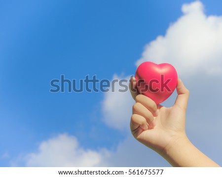 Hand giving red heart Give love to each other on a background sky and white clouds.