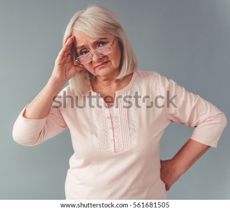 Beautiful mature woman in eyeglasses is touching her head having a headache, on gray background