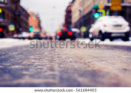 Snowy winter in the big city, the cars traveling on a green traffic light signal. Close up view from the asphalt level, image in the blue toning