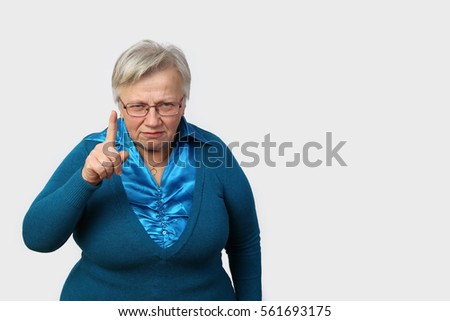 Grumpy senior woman in glasses threatens finger on gray background  with blank copy space for text - grandmother portrait Royalty-Free Stock Photo #561693175
