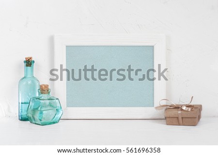 Empty wooden white frame, vintage blue glass bottles and gift box with ribbon on the white table, mock-up