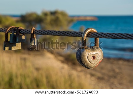 Old rusty padlocks, one of these heart shaped, hanging on bridge rope in front of beach. Love sign and romance concept. Blurred background. Horizontal.