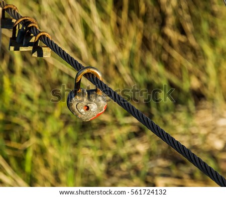 Old rusty padlocks, one of these heart shaped, as symbol of eternal love hanging on metal cable. Romance concept. Overhead view. Natural blurred background.