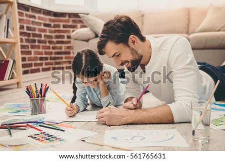 Cute little girl and her handsome father are drawing and smiling while playing together at home