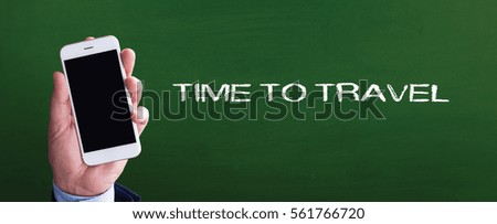 Smart phone in hand front of blackboard and written TIME TO TRAVEL