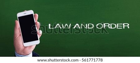 Smart phone in hand front of blackboard and written LAW AND ORDER