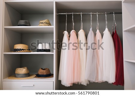 modern closet with row of white, pink, red  dress and hats hanging in wardrobe