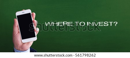Smart phone in hand front of blackboard and written WHERE TO INVEST?