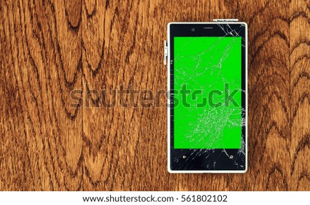 White Smartphone with broken screen on wooden table. Green chroma key display of damaged cellphone