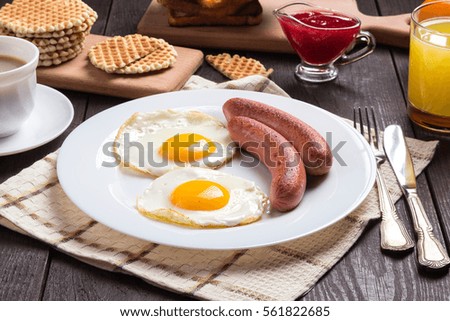 Delicious breakfast. Served on a wooden table with toast, eggs, sausage, wafers, coffee, orange juice, jam, knife, fork. Horizontal image