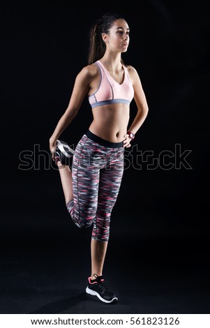 Portrait of fit and sporty young woman stretching on black background.