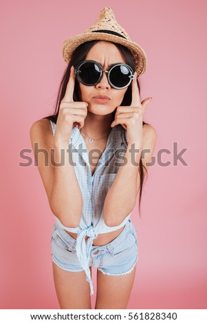 Picture of beautiful young lady wearing sunglasses and hat isolated over pink background.