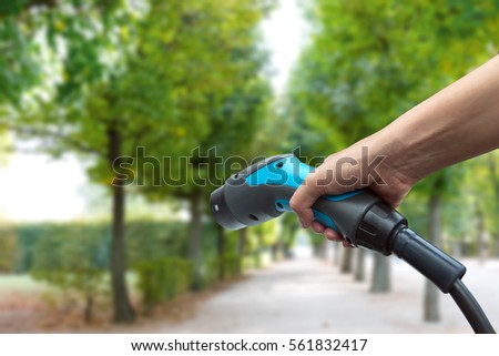 Air pollution and reduce greenhouse gas emissions concept. Hand holding and charging Electric car with green natural garden view background.
