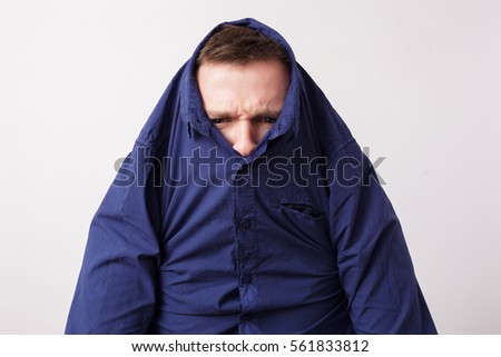Young man hiding in a blue shirt, knitting his brows angrily Royalty-Free Stock Photo #561833812