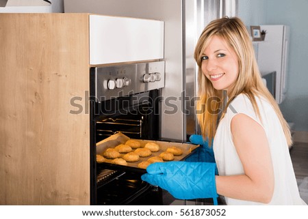 Young Smiling Woman Placing Tray Full Of Cookies In Microwave Oven At Kitchen