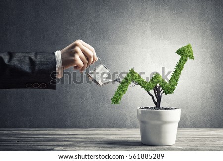 Hand of woman watering small plant in pot shaped like growing graph Royalty-Free Stock Photo #561885289