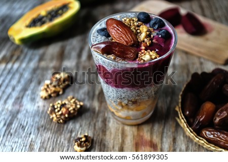 Overnight vanilla chia seeds pudding in almond milk and black sesame and beetroot dates smoothie, with fresh papaya, raw granola grains and seeds, dates, coconut crated, pomegranate and blueberries. 
 Royalty-Free Stock Photo #561899305