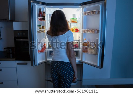 Rear View Of Young Woman Looking In Fridge At Kitchen Royalty-Free Stock Photo #561901111