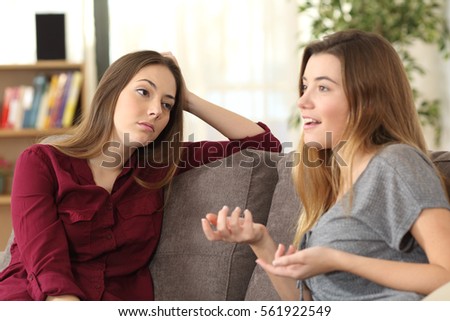 Bored girl listening to her friend having a conversation sitting on a couch in the living room at home Royalty-Free Stock Photo #561922549