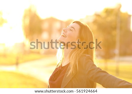 Back light portrait of a happy single teen girl breathing fresh air at sunset in a park with a warm yellow light and urban background Royalty-Free Stock Photo #561924664