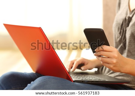 Close up of a girl hands using a phone and a red laptop sitting on the floor of the living room at home with a warm light in the background