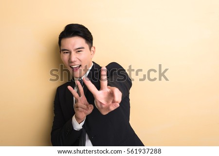 young Asian business man give you a gesture of victory, closeup portrait on studio yellow background