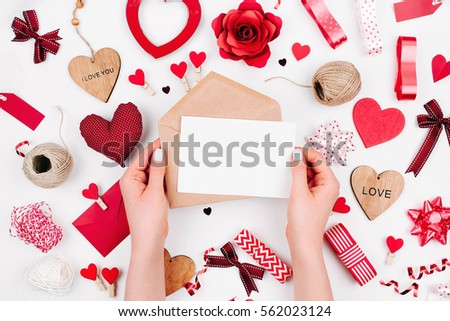 Female hands are holding a Blank white greeting card on white background with romantic decoration. flat lay