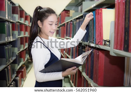  Happy smiling Asian student choosing books with bookshelves in library