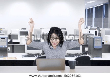 Portrait of an attractive young businesswoman looking at a laptop and raising hands up while sitting in the office