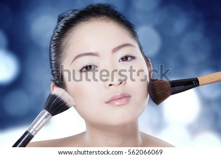 Portrait of pretty model with beautiful face, using makeup brush with bokeh background 