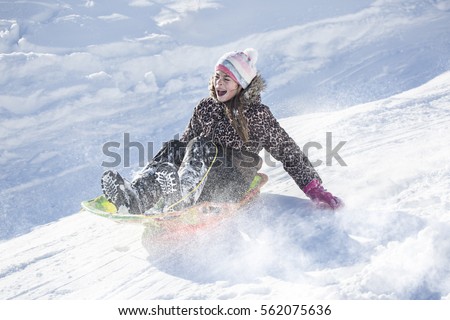 Happy and excited girl Sledding downhill on a snowy day.Cute girl laughing and showing excitement while she slides downhill while snow sledding on a winter day outdoors