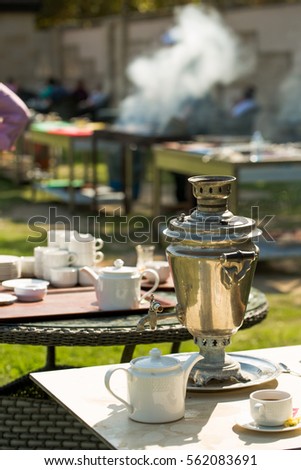 Family day outdoors with samovar tea and tea pot with barbecue smoke in the background