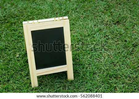 Blank black board with easel on green grass background