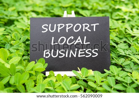 "SUPPORT LOCAL BUSINESS" word written on blackboard with green grass background.