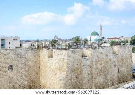 View of the citadel and mosque in the old city of Akko, Israel. Cityscape of the ancient city of Acre. Picturesque scenery of Akko's skyline, rooftops, palm trees, minaret, calm sky in the background.