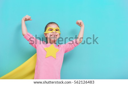 Little child plays superhero. Kid on the background of bright blue wall. Girl power concept. Yellow, pink and  turquoise colors.