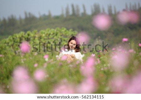 Beautiful young woman in a field of Purple, pink, red, cosmos flowers in the garden with blue sky and clouds background in vintage style soft focus.
