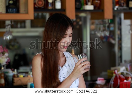 Gorgeous young Asian holding a glass of whiskey, standing in a house bar, looking downward at her glass. After work relaxation concept.