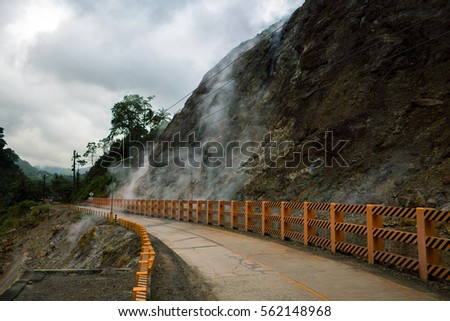 Road near geyser smoke field. Evaporation of gas from rocky mountain. Natural geyser eruption. Hot springs near active volcano. Underground geothermal energy source. Smoke field in Philippines island