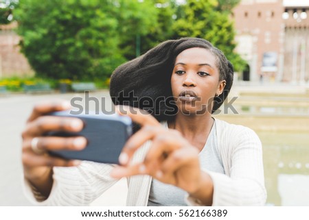 Half length of young beautiful afro black woman outdoor in the city holding a smart phone taking selfie - technology, vanity, social network concept